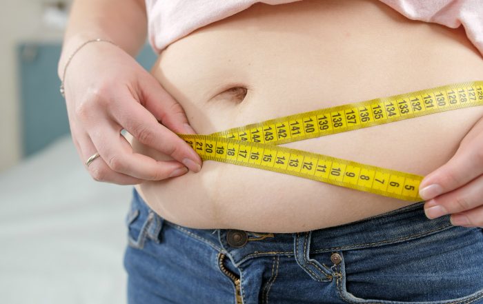 Closeup of young woman loosing weight measuring her waist. Concept of dieting, unhealthy lifestyle, overweight and obesity