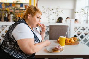 Fat woman eating doughnuts in fastfood restaurant