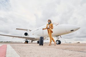 Elegant clothes. Young woman with luggage is outdoors near airplane