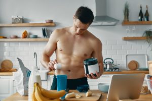 Handsome fit man preparing protein drink while standing at the kitchen