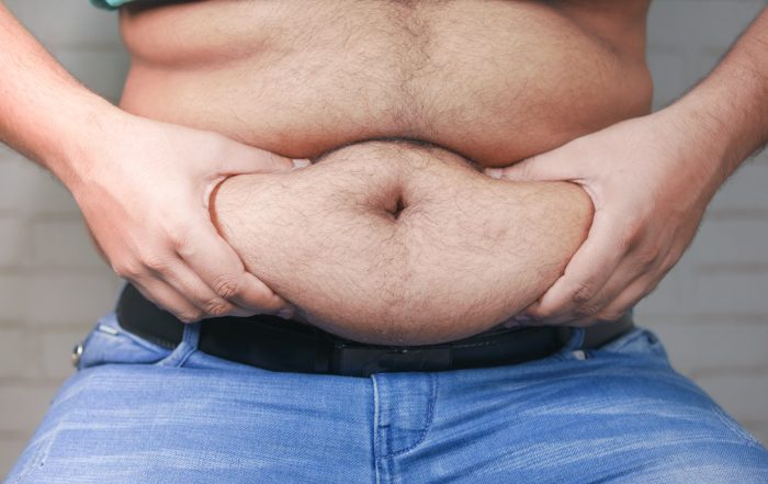 man's hand holding excessive belly fat, overweight concept