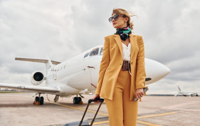 Passenger woman that is in yellow clothes, sunglasses and with luggage is outdoors near plane