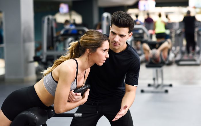 Personal trainer helping young woman lift weights