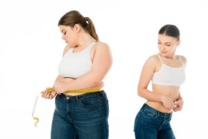 slim woman looking at sad overweight woman with measuring tape isolated on white