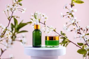 bottles for cosmetics on a white podium and branches of cherry blossoms on a pink background