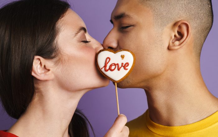 Brunette happy couple kissing while posing with heart biscuit