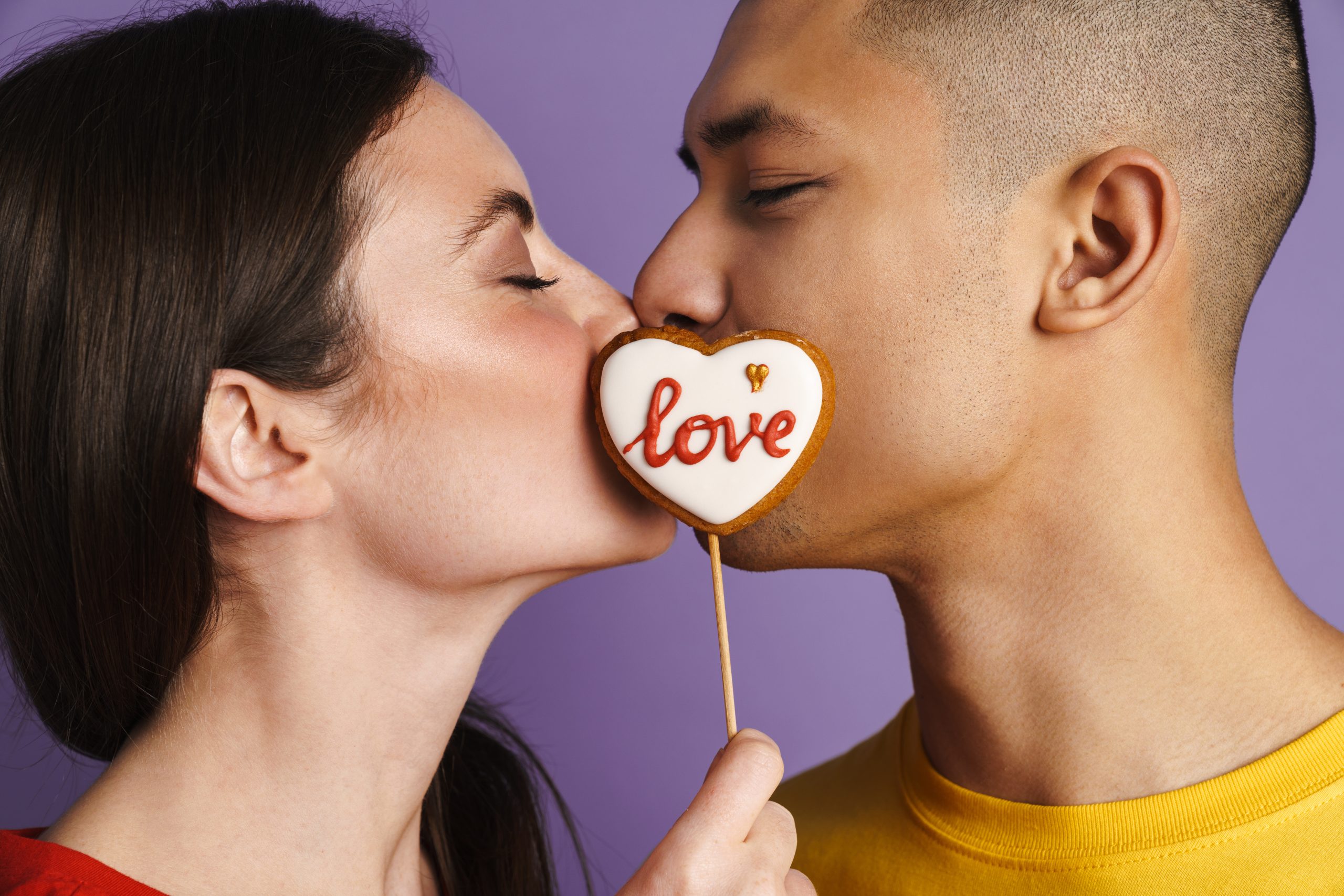 Brunette happy couple kissing while posing with heart biscuit