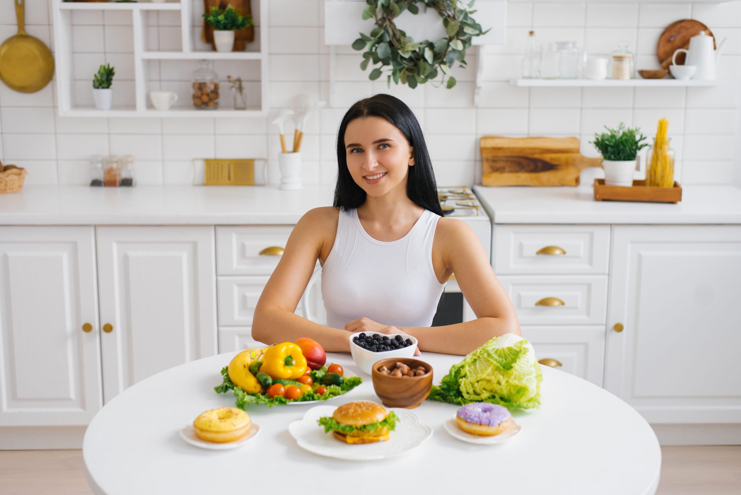 Happy healthy woman is sitting at a table with healthy food, fresh fruits and vegetables in the kitchen
