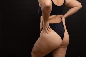 Overweight woman in black underwear pull up panties, back view. Flaunt figure imperfections, cellulite hips.
