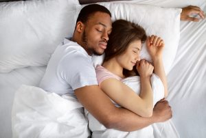 Top view of loving interracial couple sleeping in bed, hugging each other. Diverse love and relationships